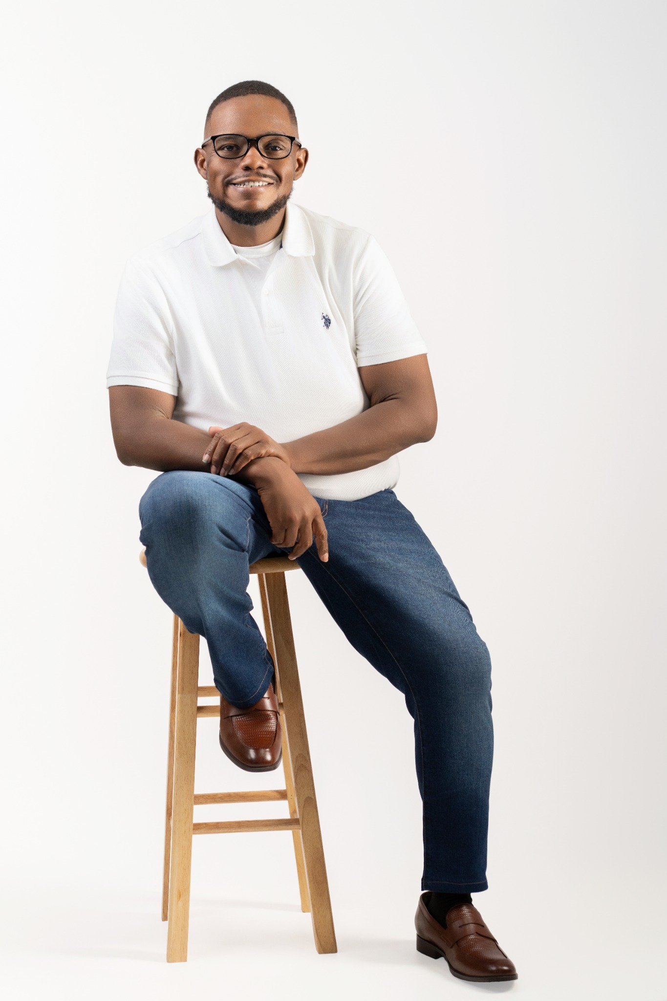 Jerome West smiling, seated on a stool in a white polo shirt